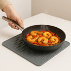 Person holding a frying pan with shrimp and vegetables on a matching mat.
