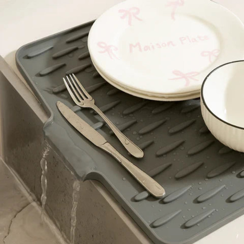 Gray dish drying mat with plates, bowls, and utensils on a kitchen counter.