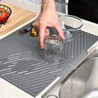 Person washing a glass on a gray dish drying mat next to a sink