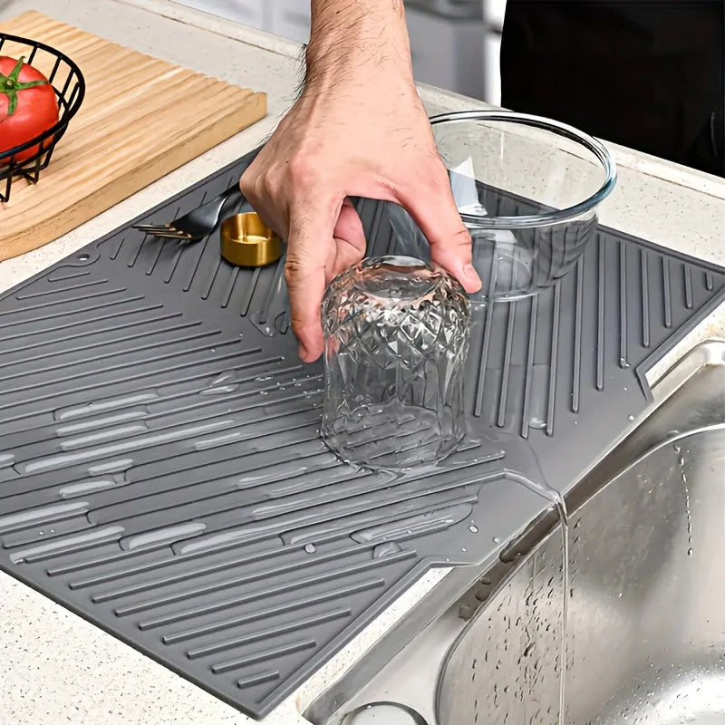 Person washing a glass on a gray dish drying mat next to a sink
