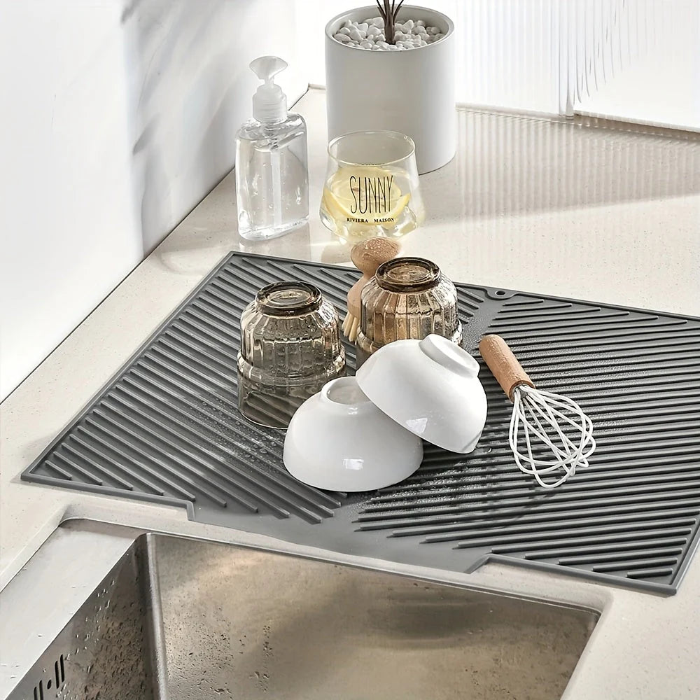 Gray kitchen mat on a countertop with various items including a white cup, whisk, and glass.