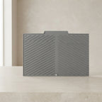 A dark gray silicone desk mat with a diagonal ribbed pattern, displayed on a light beige stone surface against a neutral beige background.