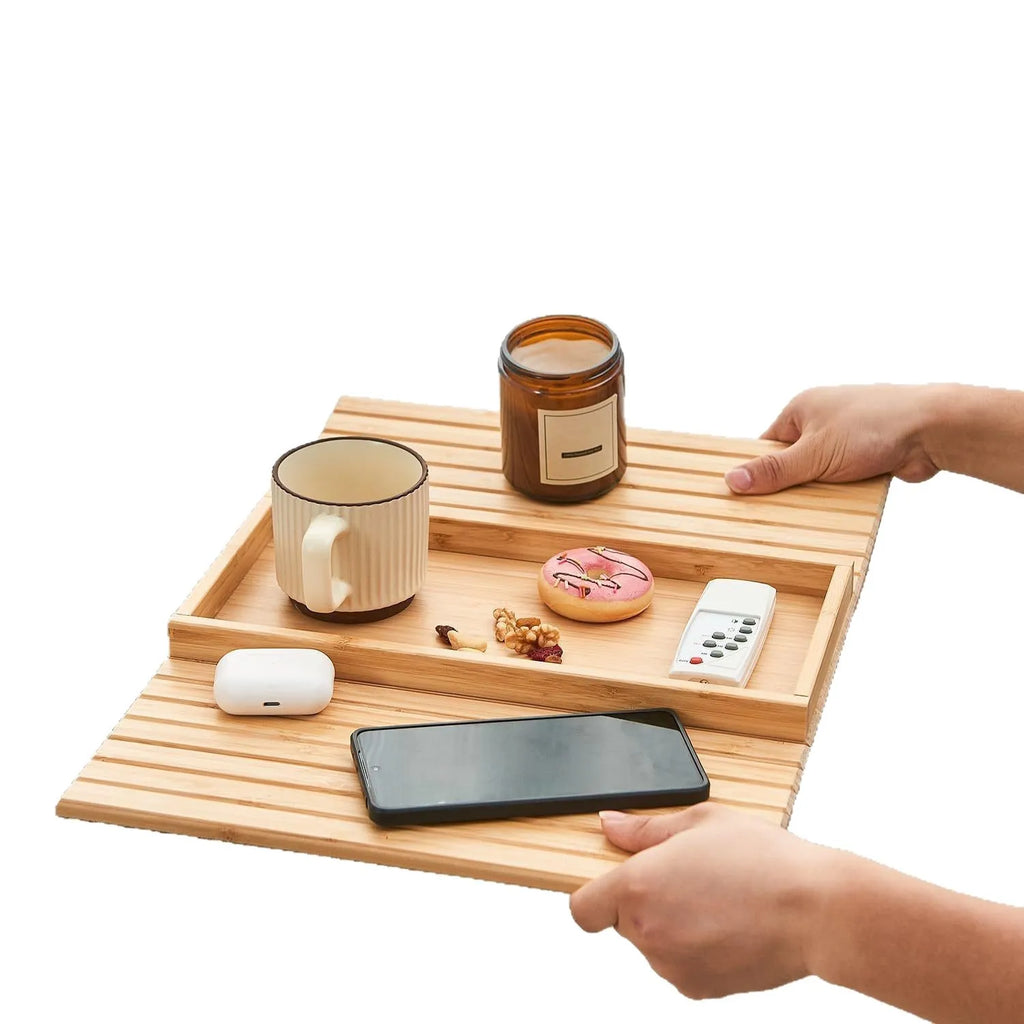Wooden tray with cup, candle, phone, and remote held by hands on a white background