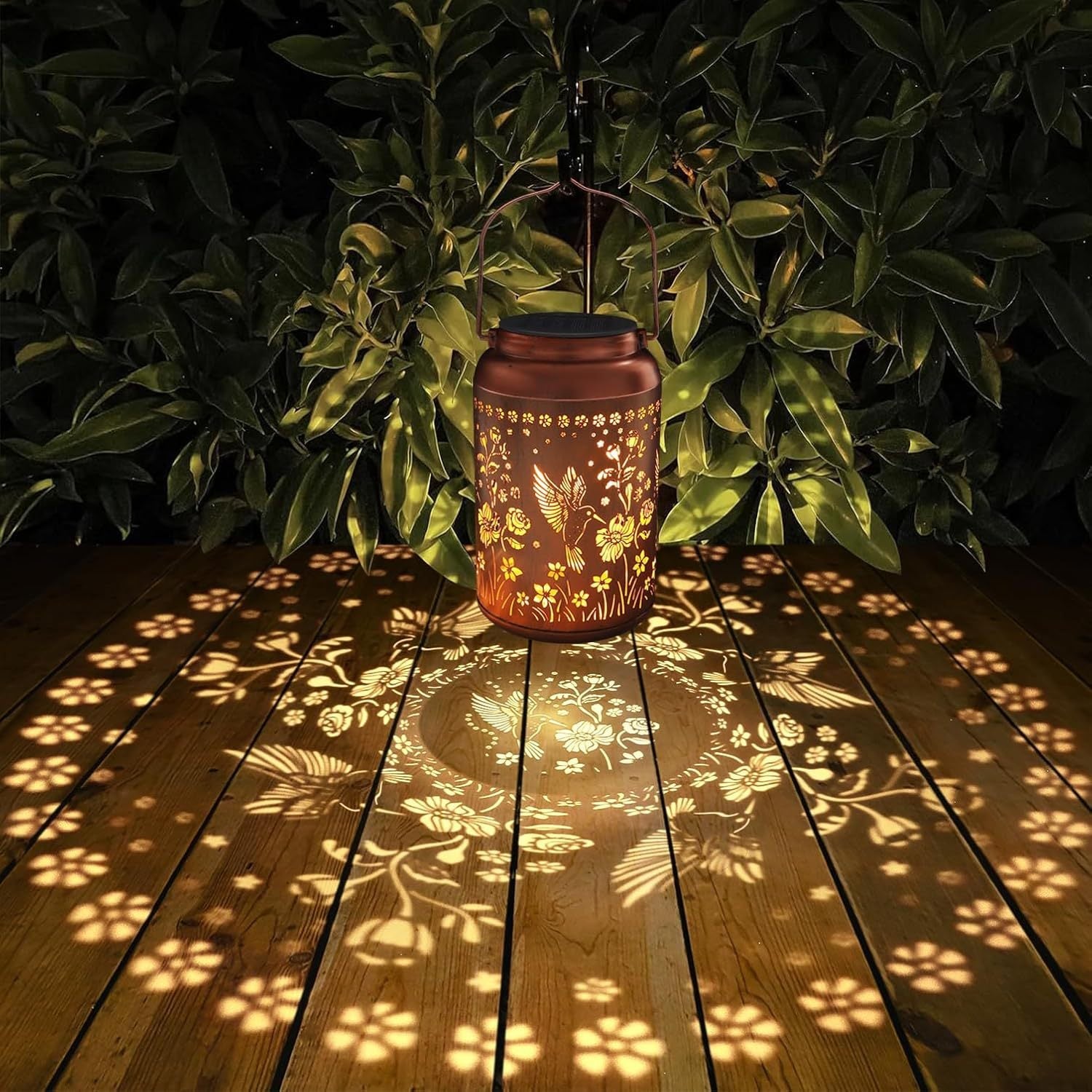 Decorative lantern casting floral shadows on a wooden deck with green foliage in the background