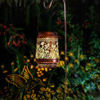 Decorative lantern with floral patterns casting shadows on a garden at night