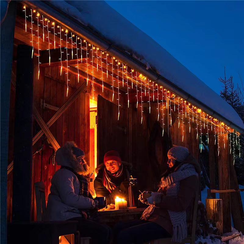 People sitting outside a wooden cabin with string lights at night