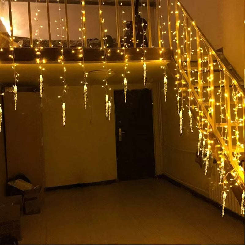 Warm white icicle string lights hanging from a staircase railing in an indoor residential setting, casting a golden glow on the walls and floor.