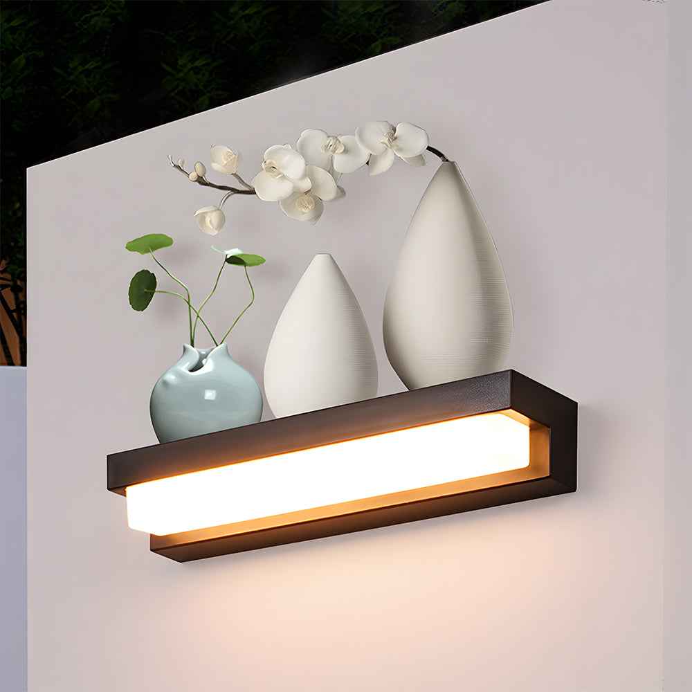 Wall-mounted light fixture with decorative vases and flowers on a white wall.