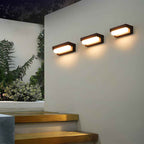 Modern outdoor wall lights on a white wall with plants in the background