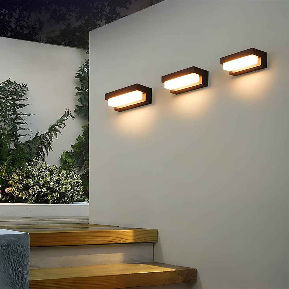 Modern outdoor wall lights on a white wall with plants in the background