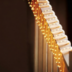 A close-up diagonal view of a stringed musical instrument, showing illuminated gold-toned strings and a light-colored headstock against a dark background.
