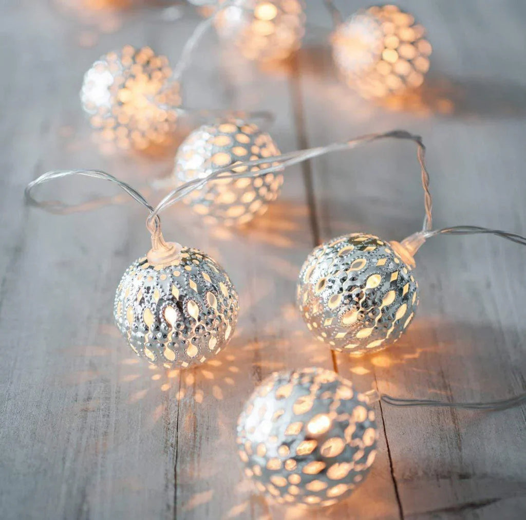 String of decorative lights with spherical metal shades on a wooden surface.