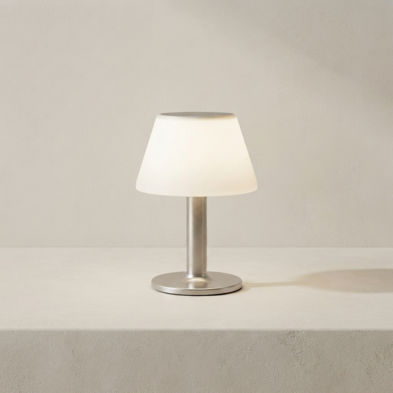 Small table lamp with a white shade and metallic base on a neutral background