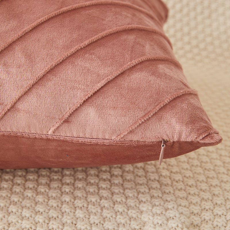 A close-up of a dusty rose velvet throw pillow with diagonal channel tufting, resting on a textured beige woven rug.