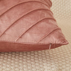 A close-up of a dusty rose velvet throw pillow with diagonal channel tufting, resting on a textured beige woven rug.