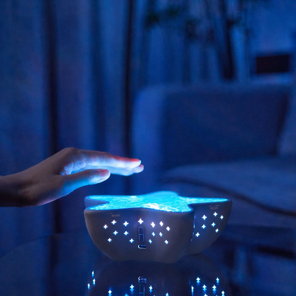 Hand reaching towards a glowing night light with star patterns in a dimly lit room.