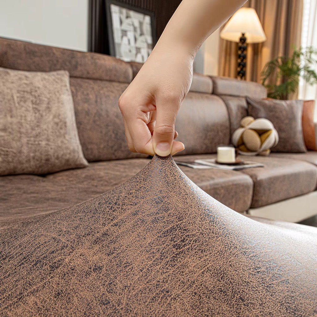 Hand holding a brown fabric swatch in front of a living room with a sofa and decor.