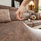 Hand holding a brown fabric swatch in front of a living room with a sofa and decor.