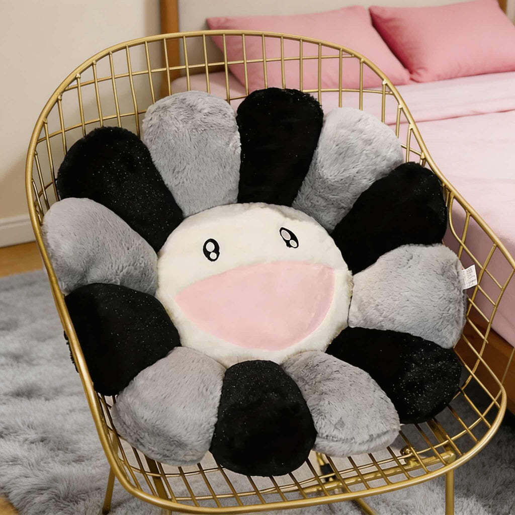 Flower-shaped plush toy with black, gray, and pink petals on a gold wire chair.