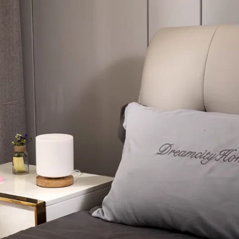 White diffuser on a nightstand next to a bed with a pillow labeled 'Dreamcity Home'.