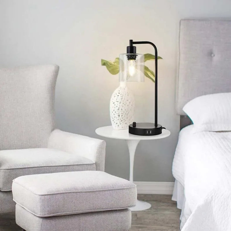 Modern bedroom with gray armchair, ottoman, and nightstand with decorative lamp.