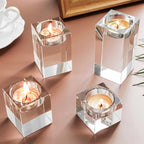 Four clear glass candle holders with lit candles on a pink surface.