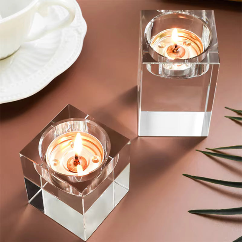 Two crystal candle holders with lit candles on a brown surface.