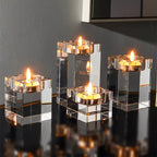 Set of four clear glass candle holders with lit candles on a reflective surface.