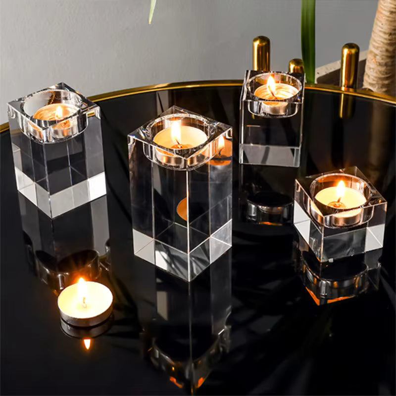Five clear acrylic square candle holders with lit tealight candles, arranged on a glossy black table with gold trim.
