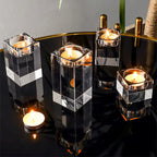 Five clear acrylic square candle holders with lit tealight candles, arranged on a glossy black table with gold trim.