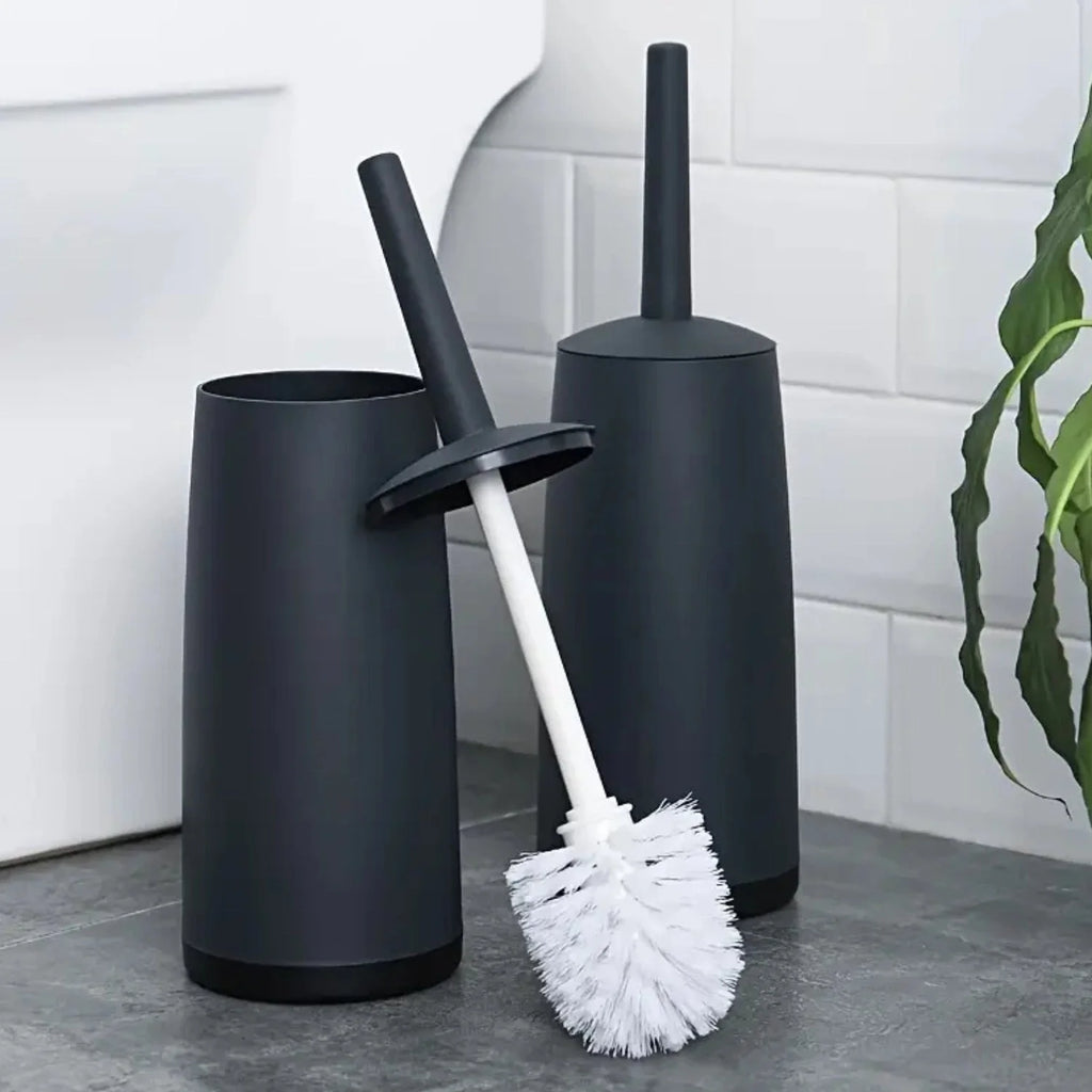 Black toilet brush holder with a white scrubbing brush on a bathroom floor.