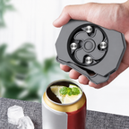 Hand holding a gray metal device over a can of soda with lemon and ice, blurred greenery in the background