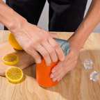Person using a manual juicer on a lemon with a wooden cutting board and ice cubes in the background.