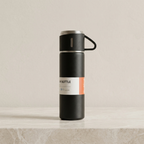 Black insulated bottle with a label on a beige surface