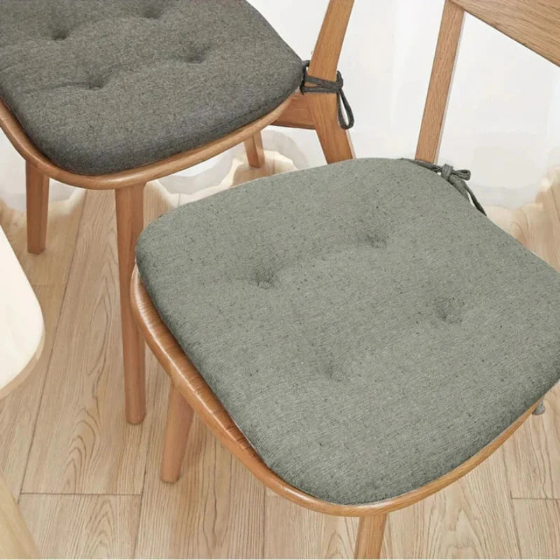 Gray cushioned chair pads on wooden chairs with a light wood floor background.