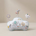 A baby sensory pillow with a cloud-shaped design, featuring a printed safari animal pattern with an elephant, lion, penguin, and rainbow. It has three hanging sensory toys: a flower, a monkey, and a smiling cloud.