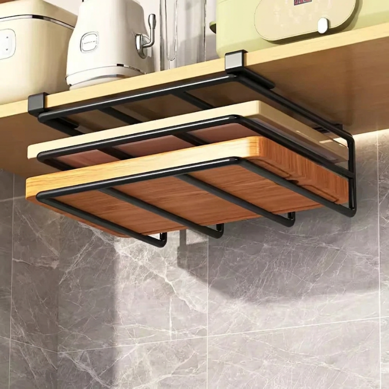 A wall-mounted black metal kitchen cutting board rack holding three wooden cutting boards, installed under a wooden countertop in a kitchen setting with gray marble tile backsplash.