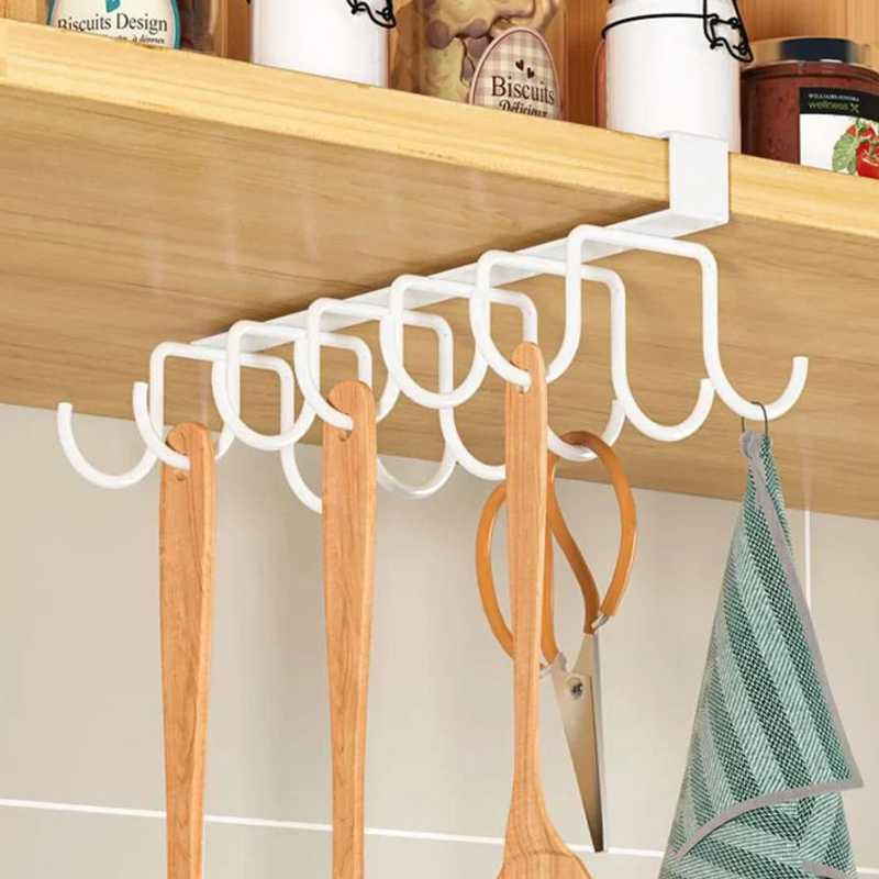 White plastic kitchen utensil hanger mounted under a wooden shelf, holding wooden spoons, scissors, and a green striped cloth.