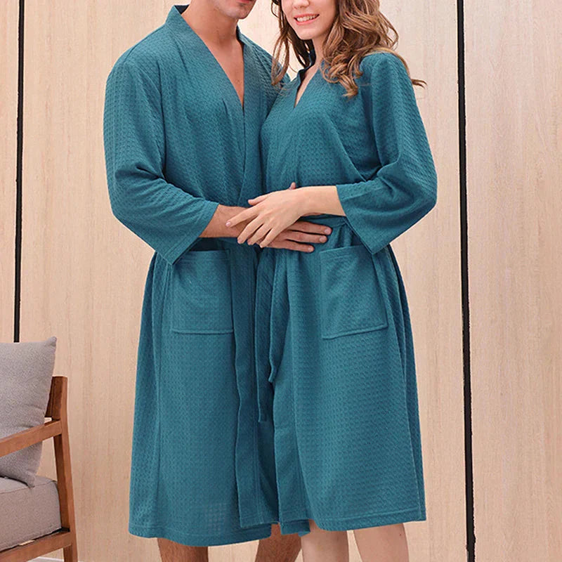 Two people wearing teal robes standing close together against a wooden panel background.