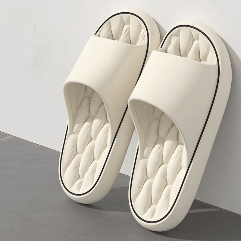 Pair of white slippers with quilted sole on a gray surface
