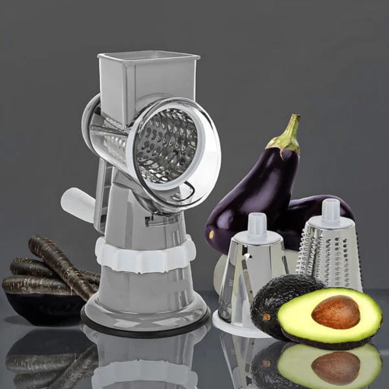 Manual grinder with grating attachments and vegetables on a reflective surface