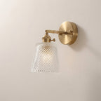 Wall-mounted light fixture with gold finish and textured glass shade on a plain wall.