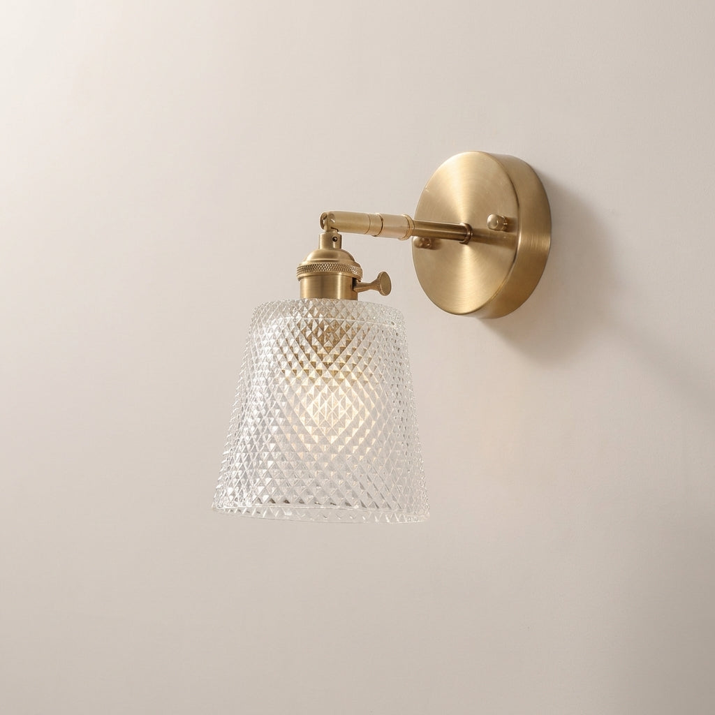 Wall-mounted light fixture with gold finish and textured glass shade on a plain wall.