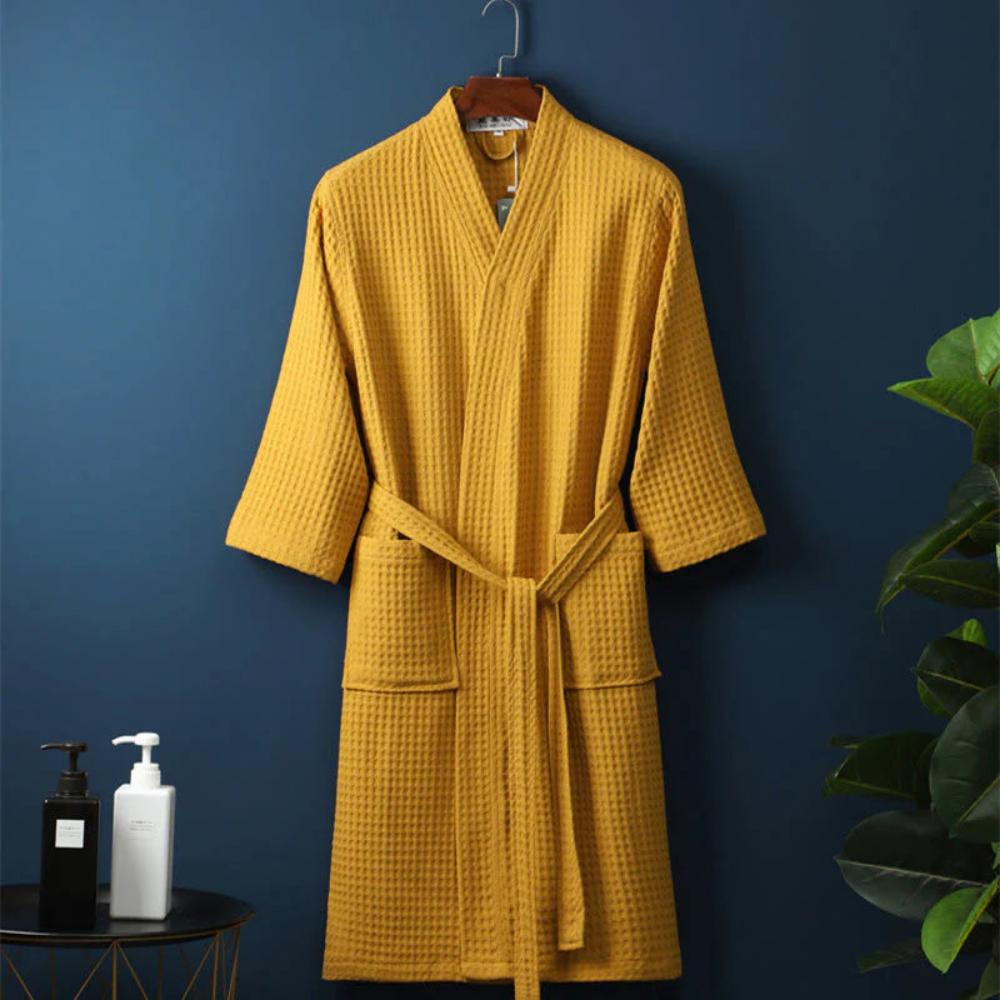 Yellow robe hanging on a hook against a blue wall with a plant and bottles in the foreground.