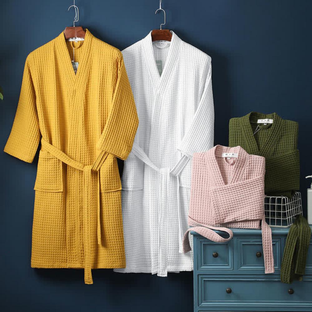 Yellow, white, and pink robes hanging on a dark blue wall with a green vest and basket.