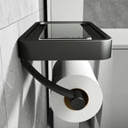 Black wall-mounted toilet paper holder with a roll of toilet paper on a tiled bathroom wall.