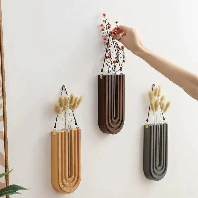 Three wall-mounted vases in different colors with plants on a white wall.