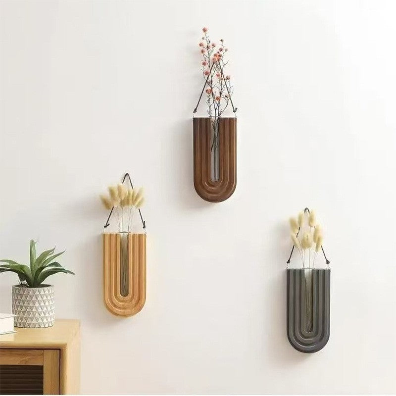 Three wall-mounted vases with floral arrangements on a light gray wall.