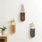 Three wall-mounted vases with floral arrangements on a light gray wall.