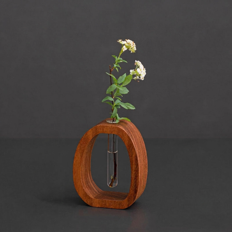 A small wooden oval-shaped vase with a clear glass tube in the center holding a delicate green plant with white flowers, set against a dark gray background.